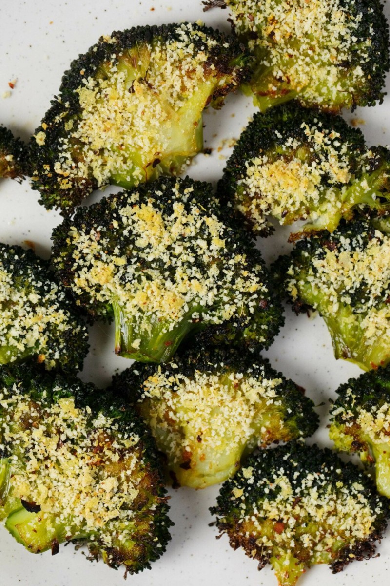 An overhead image of smashed broccoli florets that have been topped with a nut-based vegan "cheese" topping.